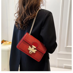 Detail of red croc-embossed crossbody bag with golden bee buckle on a black blazer