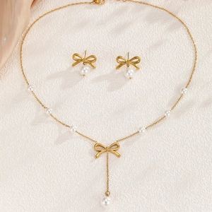 Elegant gold bow necklace and earrings set with white pearls on silk background