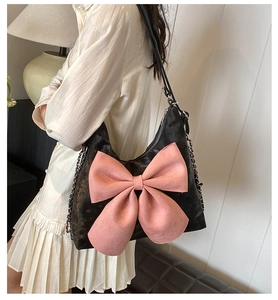 Detail view of black shoulder bag featuring a large pink bow and silver chain strap