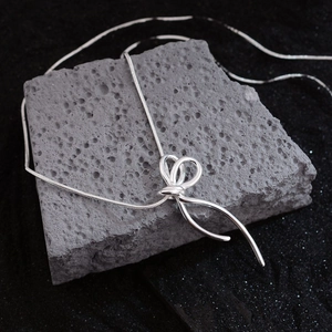 Elegant silver bow pendant on a sleek snake chain displayed on grey stone background