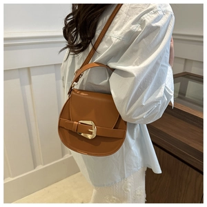 Chic brown saddle bag with gold buckle detail shown on a model in a stylish indoor setting