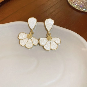 Detail of cream flower petal earrings with gold trim on a grey ceramic tray