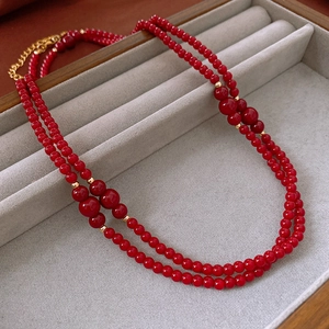 Detail of red beaded layered necklace with golden spacers on a grey jewelry display tray
