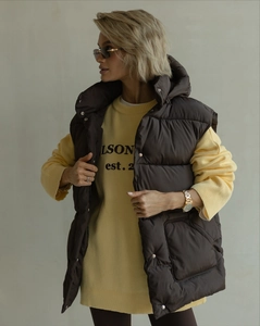 Detail of a brown hooded down vest layered over a long yellow knit sweater for autumn