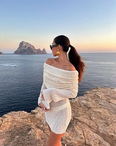 Detail of white off-shoulder long sleeve mini dress with knit texture in beach sunset