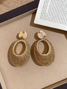 Detailed view of large gold woven metal oval earrings on a velvet jewelry display tray