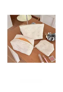 Detailed set of three white quilted shell cosmetic bags with metal zippers on wooden table
