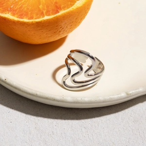 Close-up of minimalist silver irregular double-layer wave ring on orange and white plate