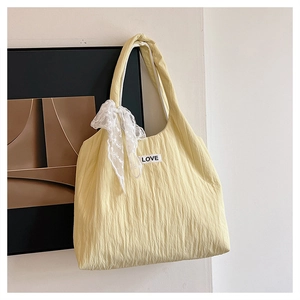 Detail of light yellow pleated tote bag featuring white lace bow and LOVE patch
