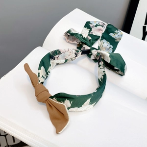 Detail of dark green floral fabric headband with brown bow knot on a white book