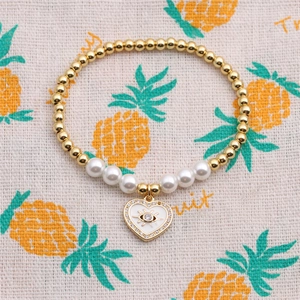 Dettaglio del bracciale con perle dorate e ciondolo cuore smaltato con occhio greco
