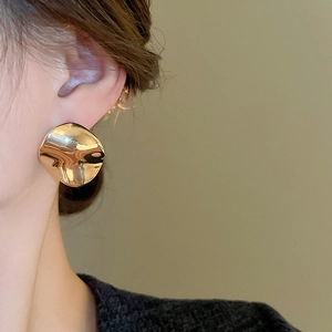 Close-up of gold-plated irregular wavy stud earring on model with high-polish mirror finish