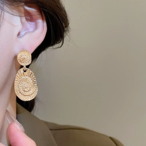 Detail shot of golden vintage swirl texture on oval metallic drop earrings worn by model