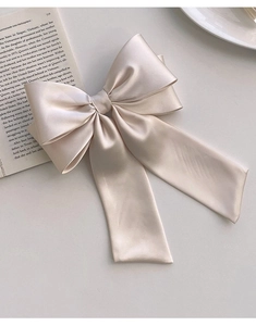 Detail of champagne satin bow hair clip placed on a book for a French elegant style