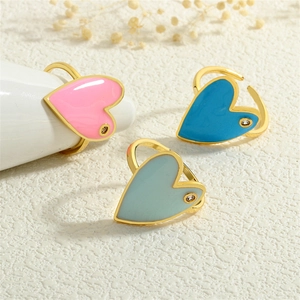 Three colorful enamel heart rings with crystals and gold plating on beige surface