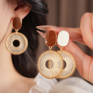 Detail of woven mesh earrings featuring brown resin and golden hoops on a soft cloth