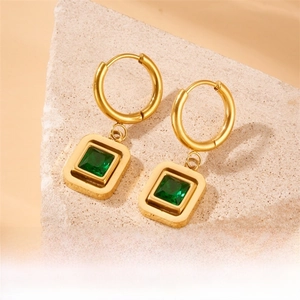 Macro view of 18K gold geometric earrings with square emerald green stones on rock