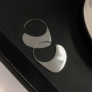 Close-up of silver geometric crescent earrings with brushed metal texture on a black tray
