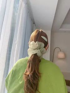 Close-up of green organza scrunchie and textured clip worn in hair on green sweater