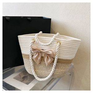 Close-up of beige woven tote bag with large decorative bow and white rope handles