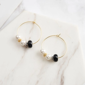 Detail of gold hoop earrings with white pearls and black obsidian beads on marble
