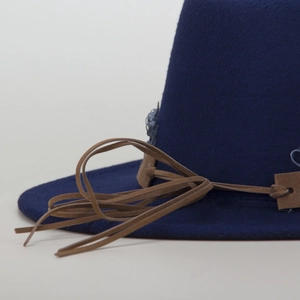 Detail of navy wool fedora hat featuring brown braided leather band and long tassels