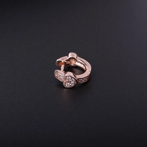 Detailed macro view of rose gold heart earring with clear zircon crystals on black surface