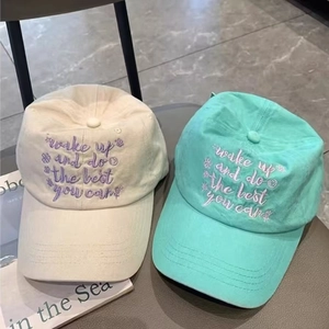 Close-up of washed cotton baseball caps with motivational embroidery in beige and mint green