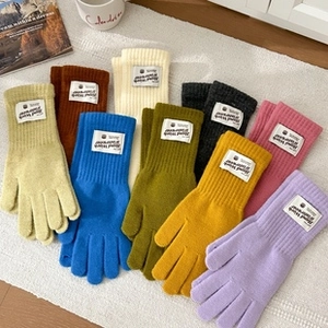 Flat lay of colorful ribbed knit gloves with handmade labels on white faux fur background