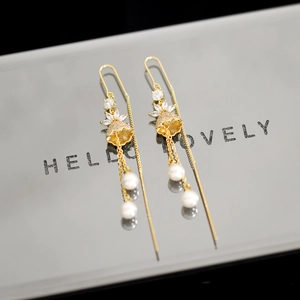 Detailed close-up of gold tassel earrings with pearls and crystal accents on a silver stand