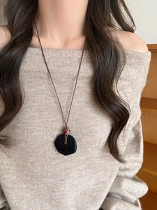 Gros plan d'un collier ethnique avec pendentif en résine et cordon ciré sur un pull