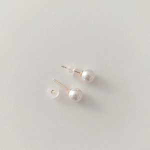 Detailed close-up of white glass pearl earrings with gold posts and silicone backs