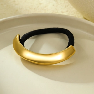 Detail of a 18k gold curved metal hair tie accessory resting on a ceramic plate