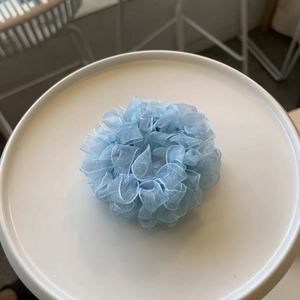 Detail view of a light blue organza scrunchie with soft pleats on a white tray