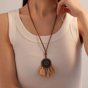 Close-up of bohemian pendant necklace with bronze mandala and beige tassels on white vest