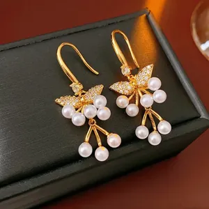 Elegante 18K vergulde vlinder oorbellen met witte parels op zwart leer achtergrond