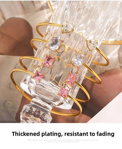 Detailed view of gold plated bangles with heart and rectangle shaped zircons on a glass vase