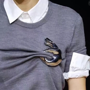 Broche vintage en forme de main argentée sur un pull en maille gris, style mode minimaliste