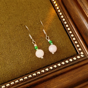 Close-up of pink quartz and green beads drop earrings with silver hooks on vintage wood