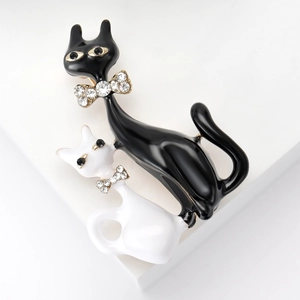 Fashionable enamel brooch featuring black and white cats with diamond bowties on white background