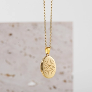Detail of gold oval locket necklace with engraved evil eye and crescent moon patterns