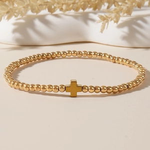 Fashionable gold beaded bracelet featuring a minimalist cross charm on a beige background