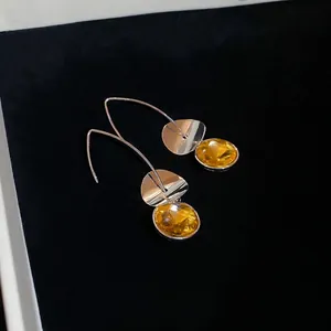 Long yellow crystal oval drop earrings with silver metal hooks on a black background