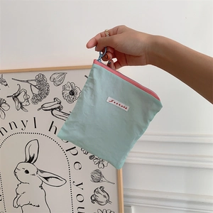 Handheld view of a mint green fabric pouch with a pink zipper and brand label