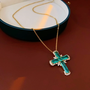 Detail of a gold necklace with a green zircon cross pendant on a warm background