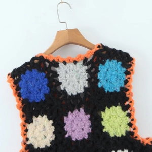 Gros plan du gilet crocheté main avec motifs floraux colorés et bordures orange vif
