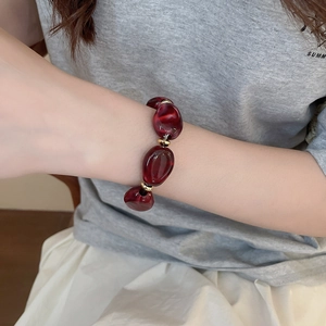 Detail of irregular dark red acrylic oval beads with golden spacers on a woman's wrist