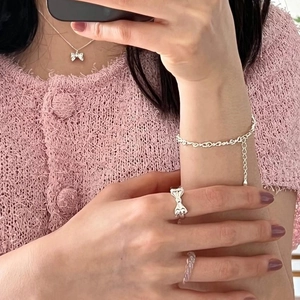 Silver bow ring and heart chain bracelet set styled on pink tweed background