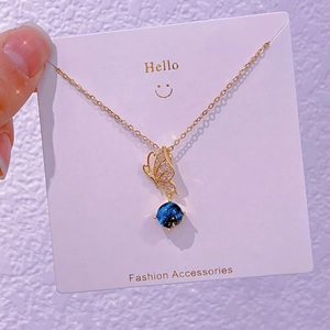 Dettaglio di un ciondolo a farfalla con sfera stellata blu su una catena in titanio oro