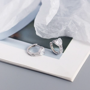 Macro shot of silver heart-shaped zircon earrings resting on an open book page